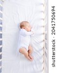 Small photo of healthy sleep of a newborn baby in a cot in a bedroom on a cotton bed, top view