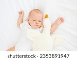Small photo of cute little newborn baby sleeping under a blanket hugging a plush goose, sweet healthy baby sleep in a white crib, a place for text.
