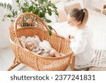 Small photo of a young mother puts her little newborn baby to sleep in a wicker cradle in the bedroom and we sing him a song, the love and care of a mother for a child, mom and baby.