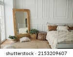 Small photo of Bright and spacious bedroom with a white wall, an eco-wooden mirror and flower pots. Cozy bright rustic style bedroom, boho style bedroom.