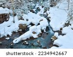 Winter landscape of a mountain river, the water slowly flows down the river bed between snow-covered stones.