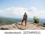 A tourist stands on top of a mountain looking into the camera, a guy with a backpack climbed a cliff, a place to camp in the mountains, a hipster on a hike, a trip to Europe. High quality photo