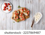 Small photo of Sandwich with cottage cheese, tomatoes and basil on white wooden background. Traditional Italian bruschetta. Healthy savory feta and tomato toast. Top view.