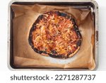 Small photo of Overcooked and burnt pizza on a tray. Top view of a home made failed pizza.