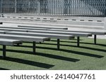 The sight of rows of empty benches neatly arranged on the lush artificial green grass, set against the backdrop of a closed and deserted presentation stage.