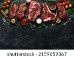 Small photo of Variety of raw aged beef steaks: t-bone, tomahawk, striploin, tenderloin, new york steak for grilling with spices on stone background. On a black stone background.