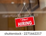 Small photo of Red sign hanging at the glass door of a shop saying: "Now hiring".