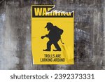 Small photo of Full-frame weathered concrete wall with a torn yellow poster in the middle depicting a troll with "Warning - Trolls are lurking around" written around.