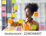 Small photo of Young Serious african american Creative team use post it notes to share idea sticky note on glass wall. Asian business people design planning and Brainstorming thinking sticky History notes concept.