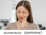 Small photo of Closing eyes asian young woman touching cheek, face expression from toothache, tooth decay or sensitivity, Having tooth or teeth problem or inflammation, suffering from health. Sensitive teeth people