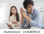 Small photo of Infidelity, suspicion asian young couple love fight relationship, wife holding cellphone, smartphone cheating on phone, scolding husband about mistrust, distrust and jealousy when sitting at home.