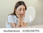 Small photo of Bored, insomnia asian young woman, girl looking at mirror, without makeup, touch under eyes with problem of dark circles, puffiness, swollen or wrinkles on face. Sleepless, sleepy people, copy space