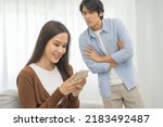 Small photo of Infidelity, suspicion asian young couple love, wife using mobile phone, husband watching spying his girlfriend while woman chat a message, man sneaky distrust and jealousy, relationship problem.