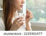 Small photo of Dietary supplement, asian young woman, girl hand holding orange medical pill, take or eat vitamin C, D for treatment for skin, hair and nail strengthen with glass of pure water at home, healthcare.
