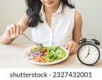 Small photo of Intermittent fasting with clock, health asian young woman, girl weight loss, eating green fresh vegetable salad on dish, plate with eat healthy of breakfast food in morning, lunch on a table at home.