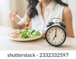 Intermittent fasting with clock, health asian young woman, girl weight loss, eating green fresh vegetable salad on dish, plate with eat healthy of breakfast food in morning, lunch on a table at home.