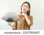 Suffering summer heat stroke, hot weather, tired asian young woman, girl sweaty and thirsty, refreshing with hand in blowing, wave fan to ventilation when temperature high at home, house on background