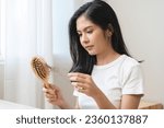 Small photo of Serious asian young woman holding brush holding comb, hairbrush with fall black hair from scalp after brushing, looking on hand worry about balding. Health care, beauty treatment, hair loss problem.