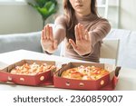 Small photo of Diet concept, unhappy asian young woman, girl refusing to eat Pizza in box at home, hand pushing away, deny junk or fast food, fighting to keep it from getting fat. Healthy nutrition of weight loss.