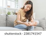 Small photo of Health care foot pain, suffering asian young woman hand rubbing, massaging sore feet area pain, sitting on sofa at home. Discomfort painful feet ache from walking for long. Physical injury.