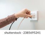 Small photo of Hand of woman plugged in, unplugged electricity cord cable at home, put on or remove electric plug cable in socket on wall outlet for saving, control power electrical energy, eco environment concept.