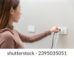 Small photo of Asian young woman plugged in, unplugged electricity cord cable, put on or remove electric plug cable in socket on wall home outlet for saving, control power electrical energy, eco environment concept.