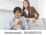 Small photo of Infidelity, suspicion asian young couple love, husband using mobile phone, wife spying his boyfriend while man chat a message, woman sneaky distrust and jealousy, relationship problem.