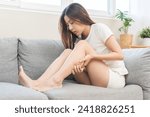 Small photo of Muscle pain or leg pain, suffer asian young woman, girl hand massaging brawn leg calf muscle cramps or spasm, trauma from inflammation of tendon at calves while sitting on sofa. Health care concept.
