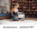 Young woman short hair wearing eyeglasses sitting on fluffy carpet with cup of hot coffee and laptop working online concentrated freelance side hustle