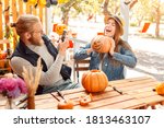 Two cheerful and rejoiced young adult friends making decoration for halloween, holding carved pumpkin in hands, taking self portrait on modern smartphone, sitting outdoor