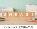Small photo of Wooden blocks with "UNEASE" text of concept, pens, notebooks, and books.
