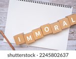 Small photo of Wooden blocks with "IMMORAL" text of concept, a pen, and a notebook.