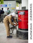Small photo of New Delhi, India-April 22 2022: Close view of red Indian post box on street, Postman delivering the mail. postman as he collects the mail from a letter box