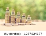 Small photo of Government income tax collection concept : Tax burlap bags on rows of rising coins, depicts the levying of taxes that aims to raise revenue to fund governing or alter prices in order to affect demand