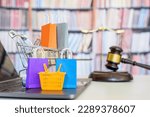 Consumer rights and consumer protection, business law concept : Shopping basket, shopping bags and  a shopping cart on a laptop computer with judge gavel, balance sale of justice and bookshelf behind.
