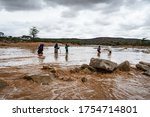 Small photo of Bokolmayo, Dollo Ado, Somalia Region, Ethiopia - 10/26/2018: Somali family in dangerous river crossing by food during heavy flooding and flash flood in dry river bed with dramatic sky.