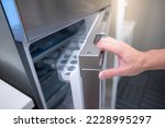 Male hand opening fridge or refrigerator door in kitchen showroom. Buying appliance for home interior design.