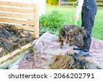 Small photo of A gardener wearing plastic boots and overalls is turning a compost pile using a shovel or fork. the worker transfers partially composted material from heap onto tarp for aeration.