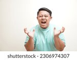 Small photo of Portrait of young Asian man wearing t-shirt rending his hair, screaming with close eyes and wide open mouth, holding hands on head. Isolated image on white background. People's emotion concept