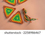 Small photo of Some multicolored triangle crochet motifs and a bundle of multicolored crochet cords on beige background. Concept of crocheting in green and orange tones.