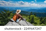 Small photo of Hiker girl sitting on a cliff edge enjoying scenic summer view. Woman relaxing on top of autumn mountain, over the clouds. Blue Ridge Parkway ,near Asheville, North Carolina, USA.