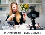Small photo of Beauty blogger woman filming daily make-up routine tutorial near camera. Influencer girl live streaming cosmetics product review. Vlogger female recommends eye shadow palette showing thump up sign.