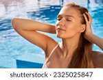Pretty woman relaxing and sun bathing near swimming pool at luxury spa. Beautiful serene young female model on holiday travel resort enjoying vacation. Sun protection concept. Wellness beach club.