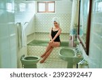 Small photo of Woman in vintage bathroom relaxes after a bath, wrapped in towel, self-care routine. Classic design, ceramic tiles echo timeless style, step-in tub, pedestal sink in an old-fashioned home setting.