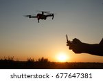 Man holds remote controller with his hands while copter is flying on background. Drone hovers behind the pilot on suset. No face