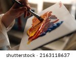Small photo of Female Artist Works on Abstract Oil Painting, Moving Paint Brush Energetically She Creates Modern Masterpiece. Dark Creative Studio where Large Canvas Stands on Easel Illuminated. Low Angle Close-up