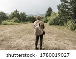Back view of tourist man with a backpack standing ready to travel on green forest background. Stalker in the post-apocalyptic world.