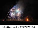 Structure with pyrotechnics and fireworks exploding and sparks during a celebratory night. People looking for a firework display with a bonfire during new years. Festival and celebration.