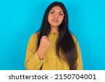 Small photo of young latin woman wearing yellow shirt over blue background shows fist has annoyed face expression going to revenge or threaten someone makes serious look. I will show you who is boss