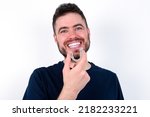 Young caucasian man wearing black T-shirt over white background holding an invisible aligner ready to use it. Dental healthcare and confidence concept.
